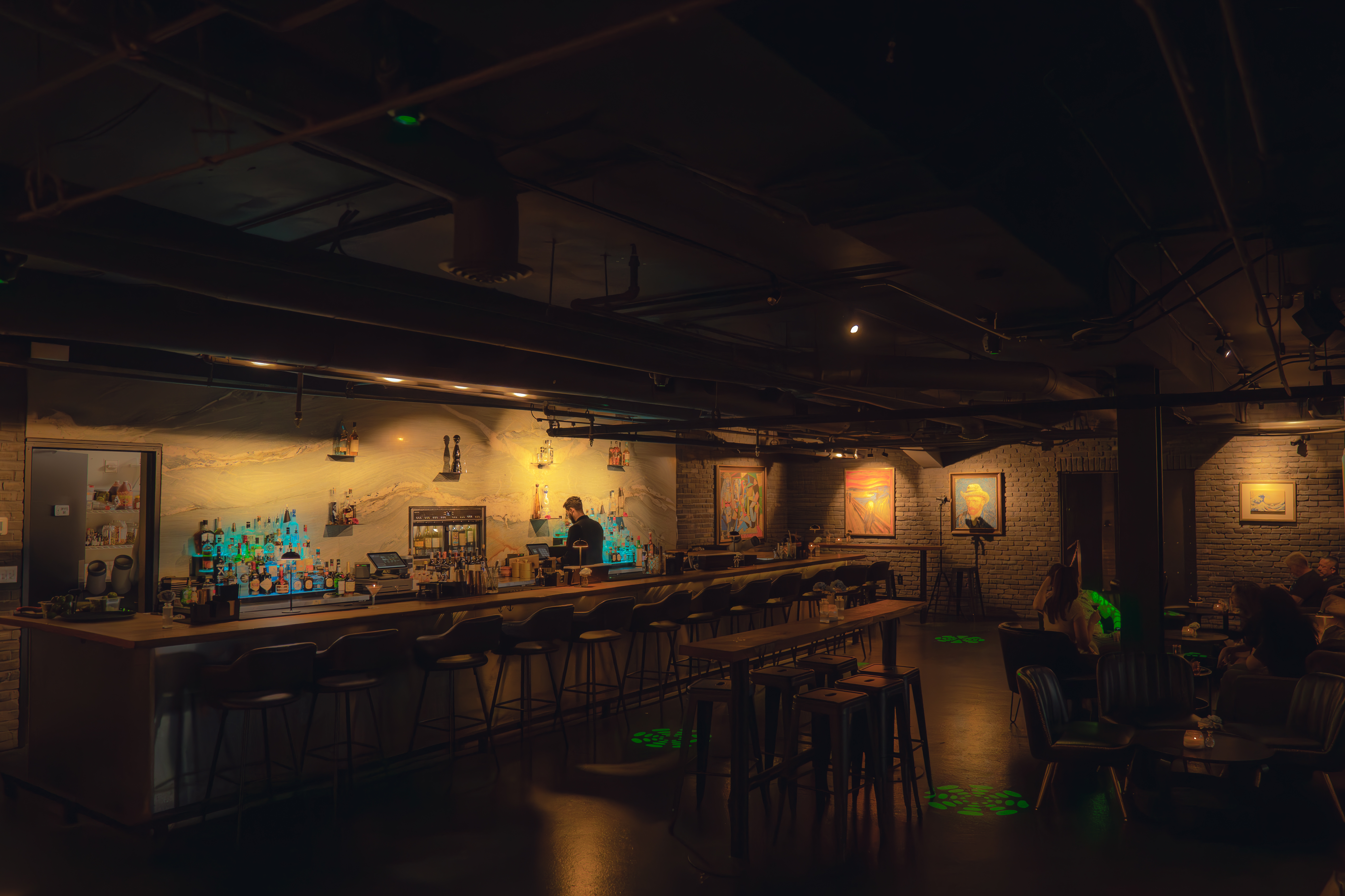Wide view of The Bunker cocktail lounge interior with backlit bar and framed art, Austin TX