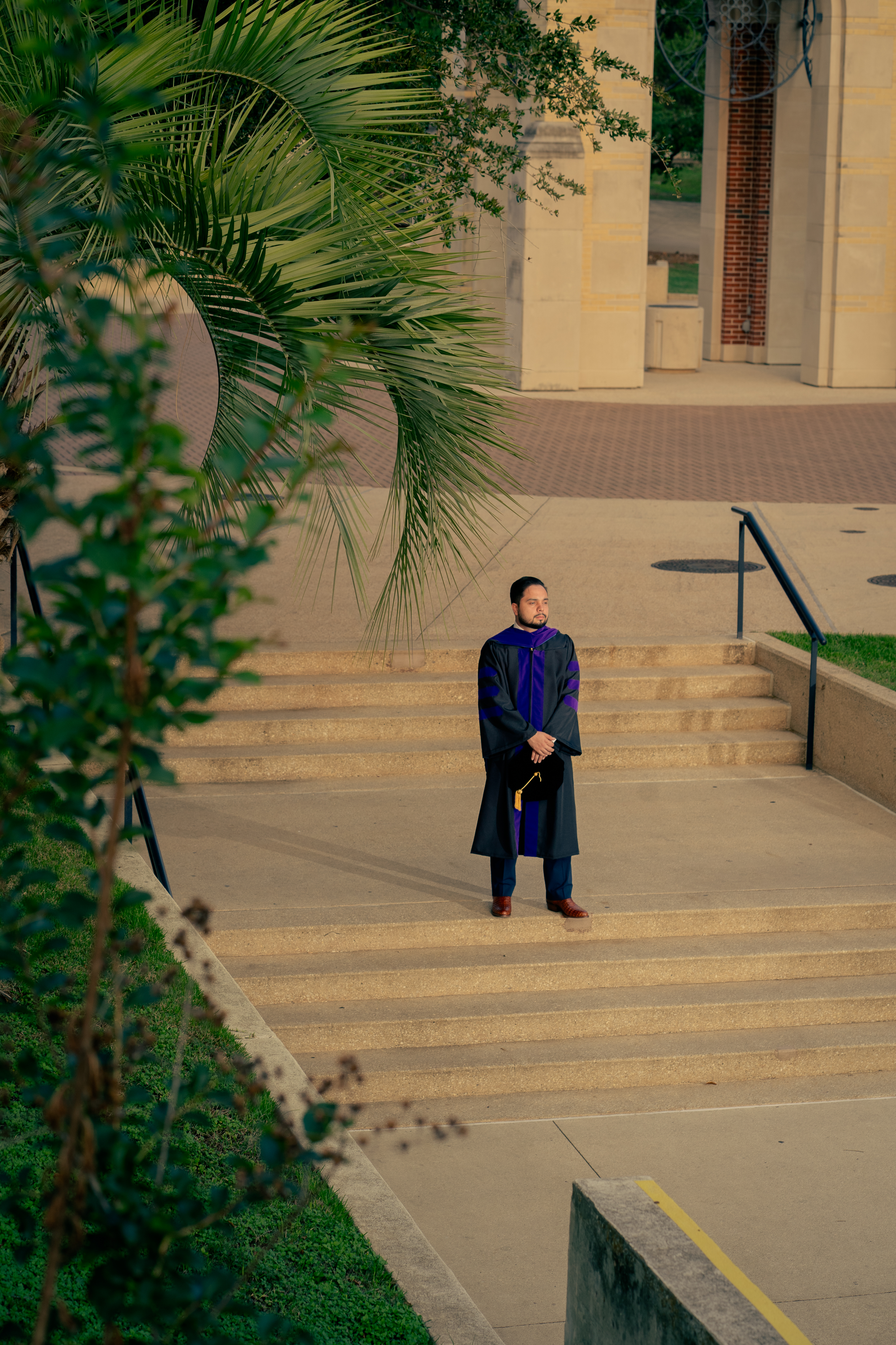 Graduate standing on campus steps framed by palm fronds at golden hour, St. Mary's University