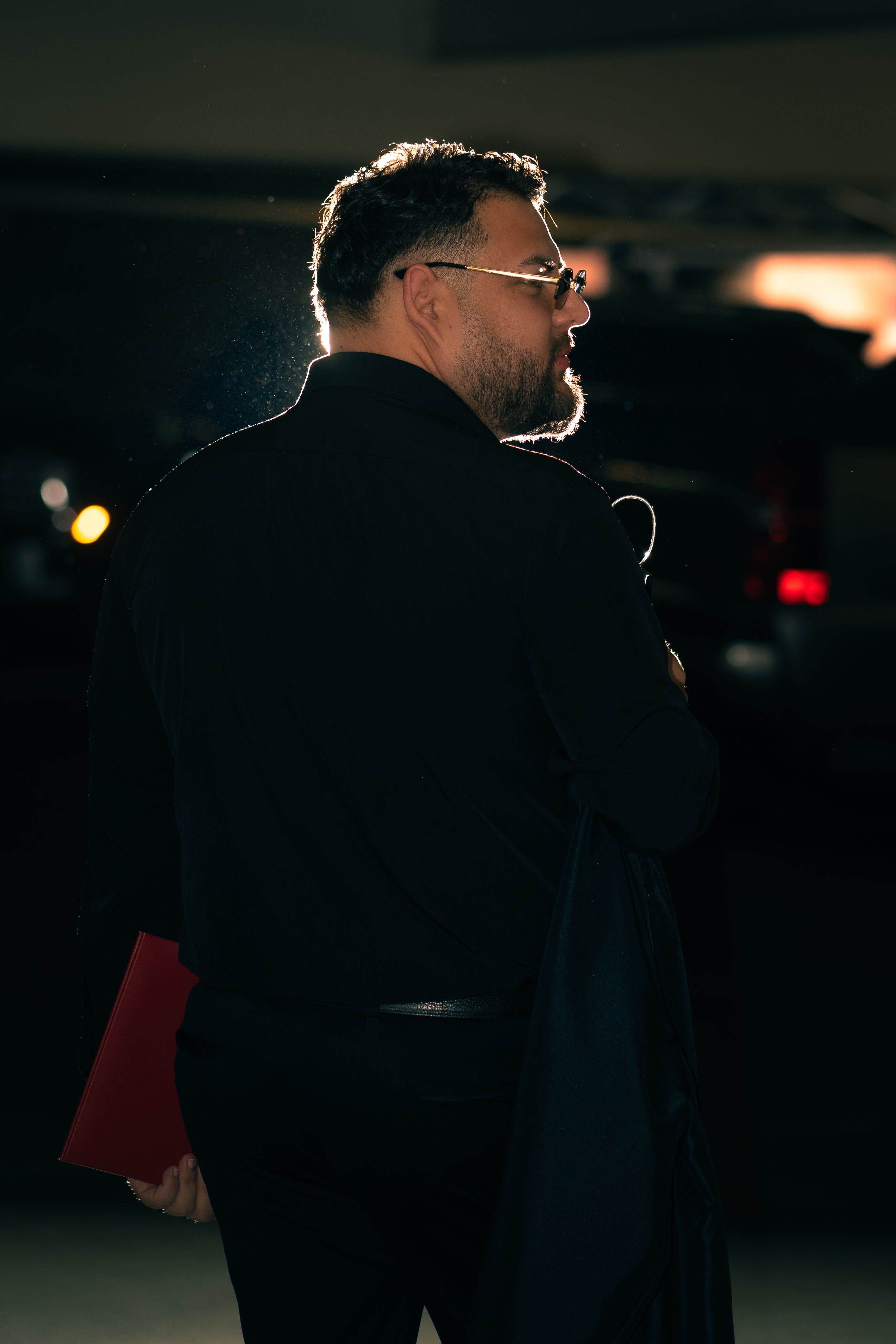 Backlit profile of graduate holding a red diploma folder at night, dramatic rim lighting
