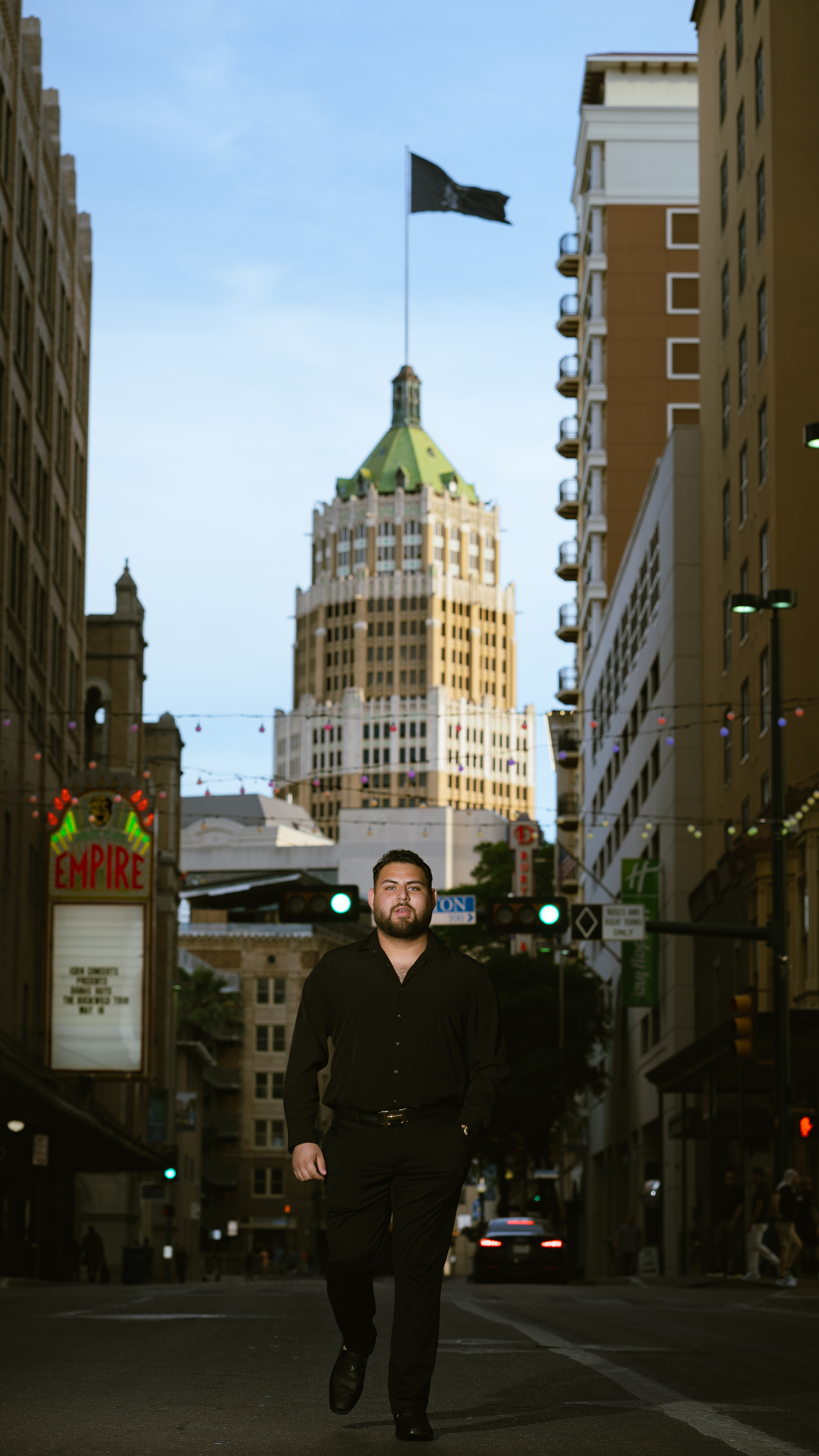 Graduate walking down a downtown San Antonio street with the Tower Life Building and Empire Theatre marquee behind him