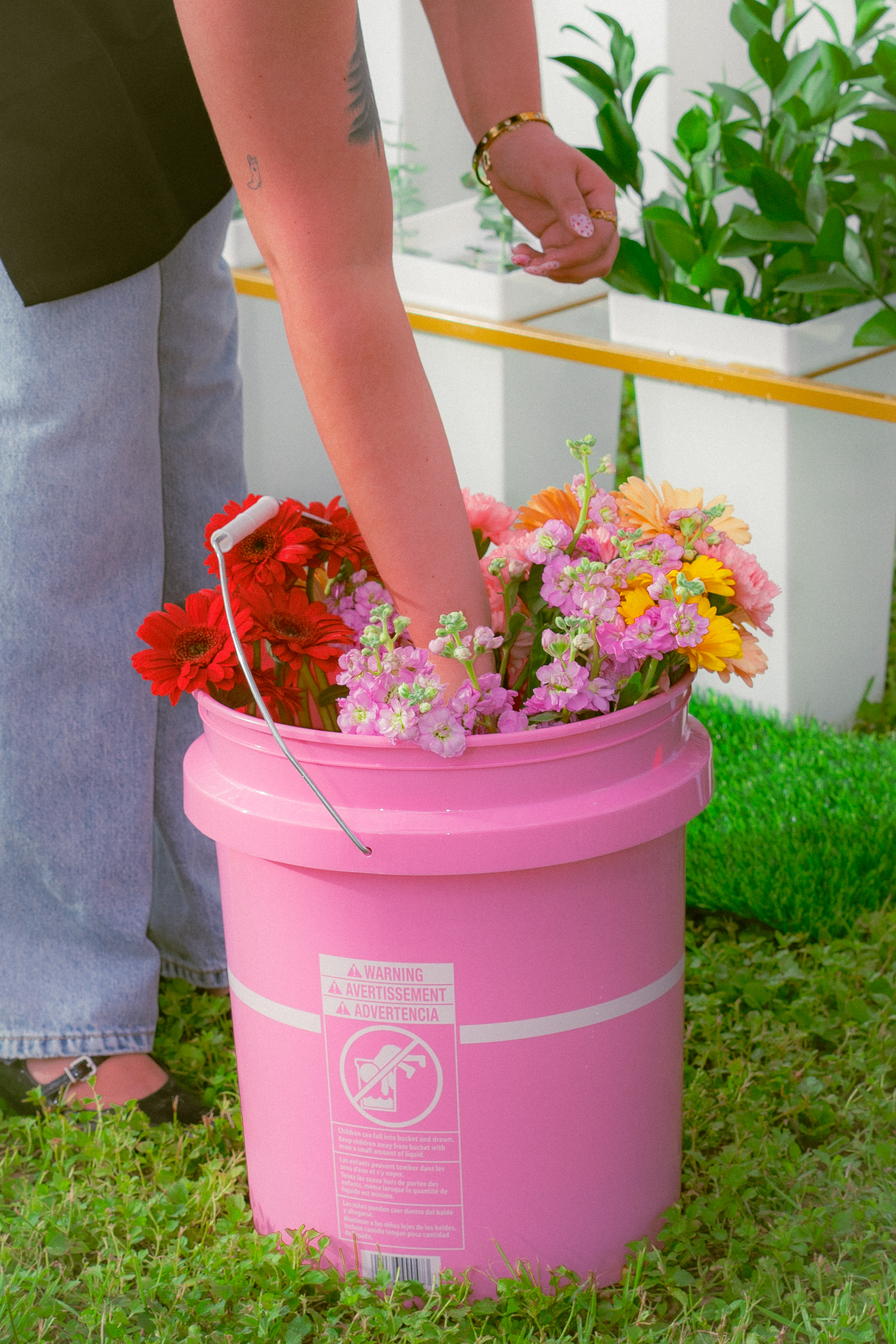 Hand reaching into a pink bucket of fresh-cut flowers at the Haus of Petals bloom bar, Austin TX
