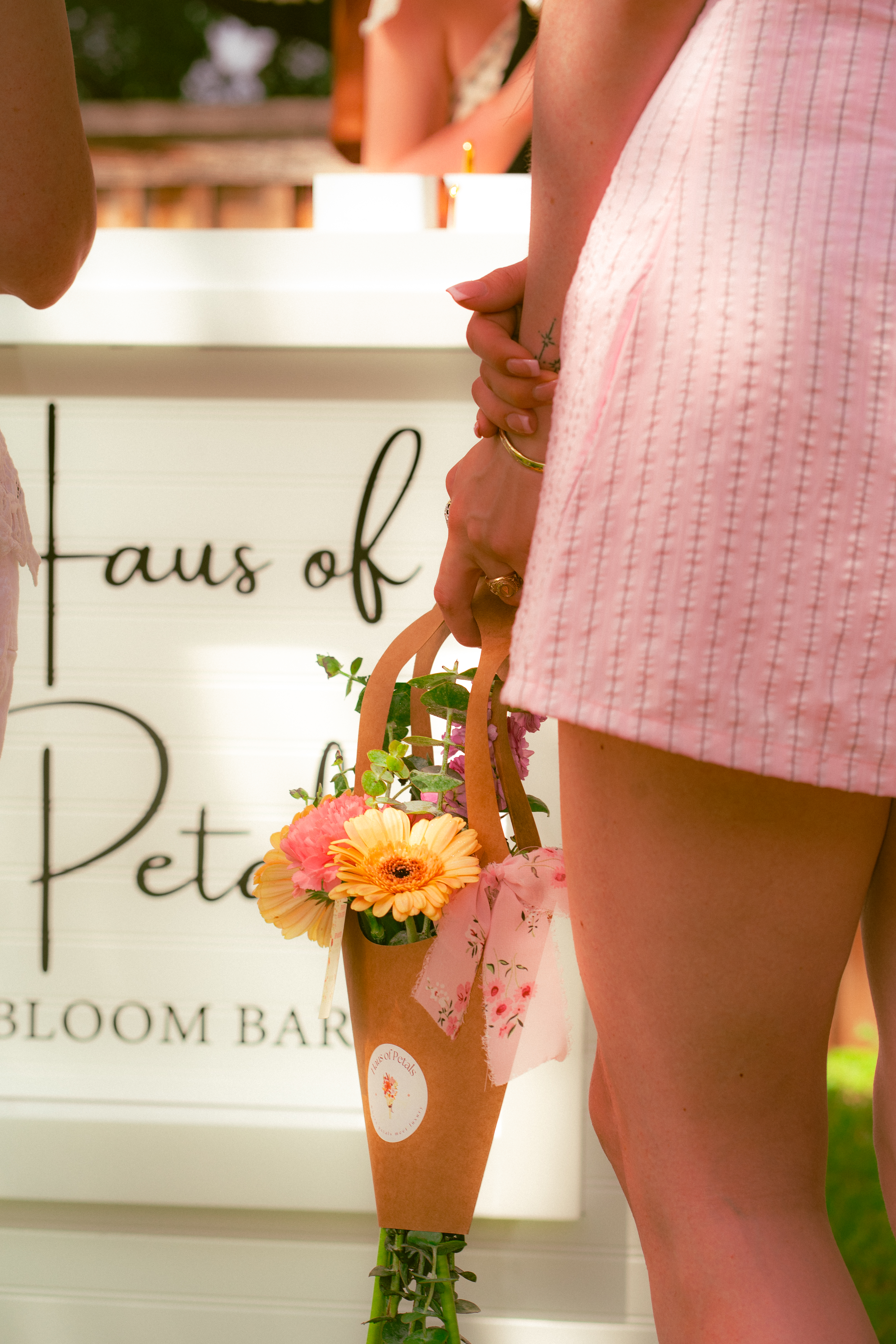 Guest holding a Haus of Petals bouquet bag beside the Bloom Bar sign