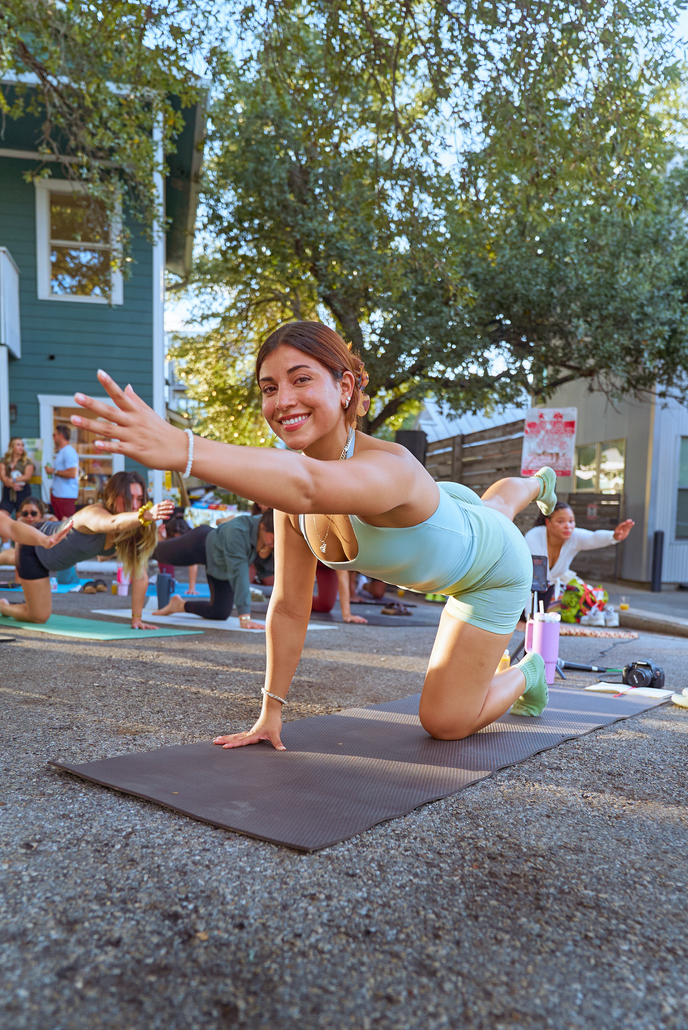 Smiling participant in a bird-dog pose on her mat during the street pilates class